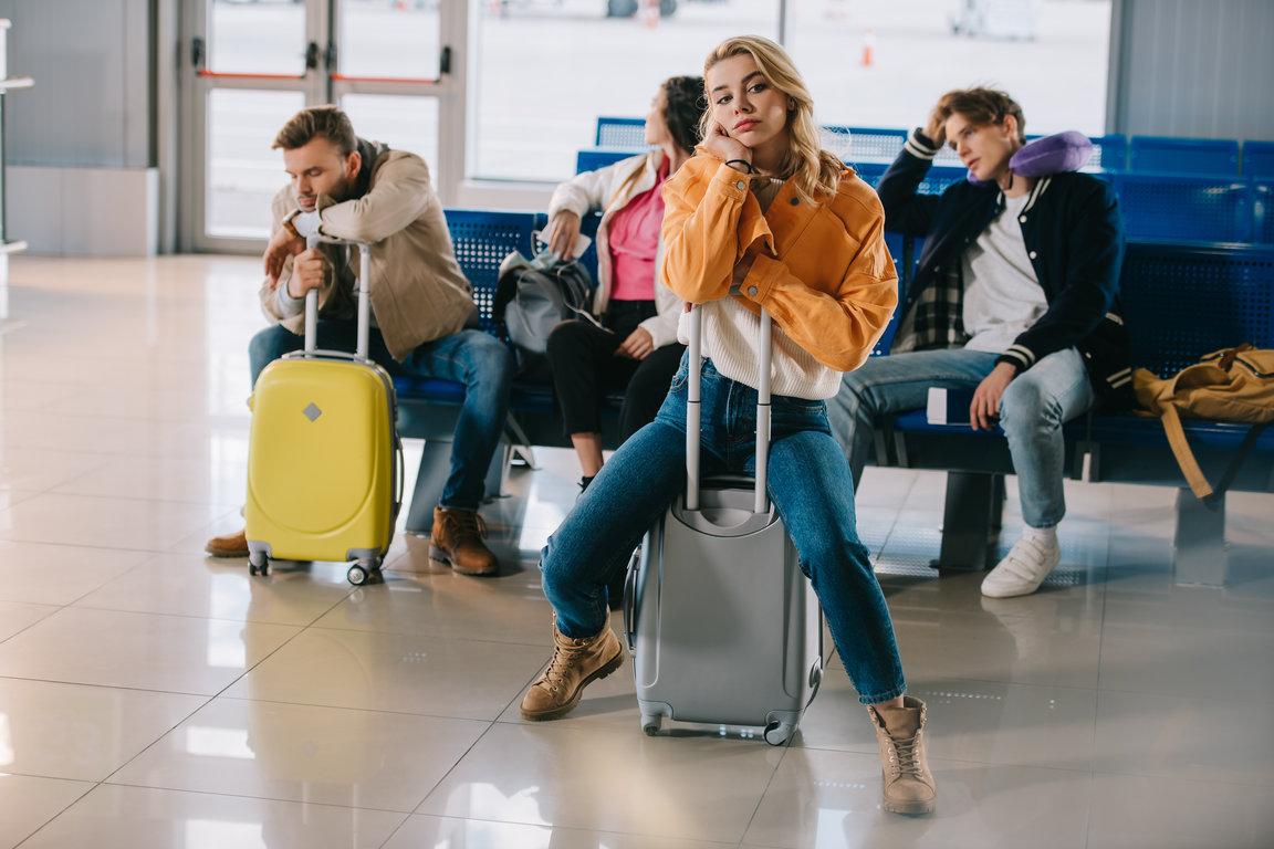 Bored young people sitting with luggage waiting for their flight in the airport terminal.
